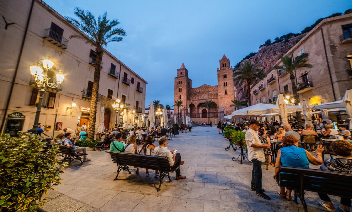 Piazza Duomo in Cefalù at dusk, with the cathedral and the Rocca behind it.