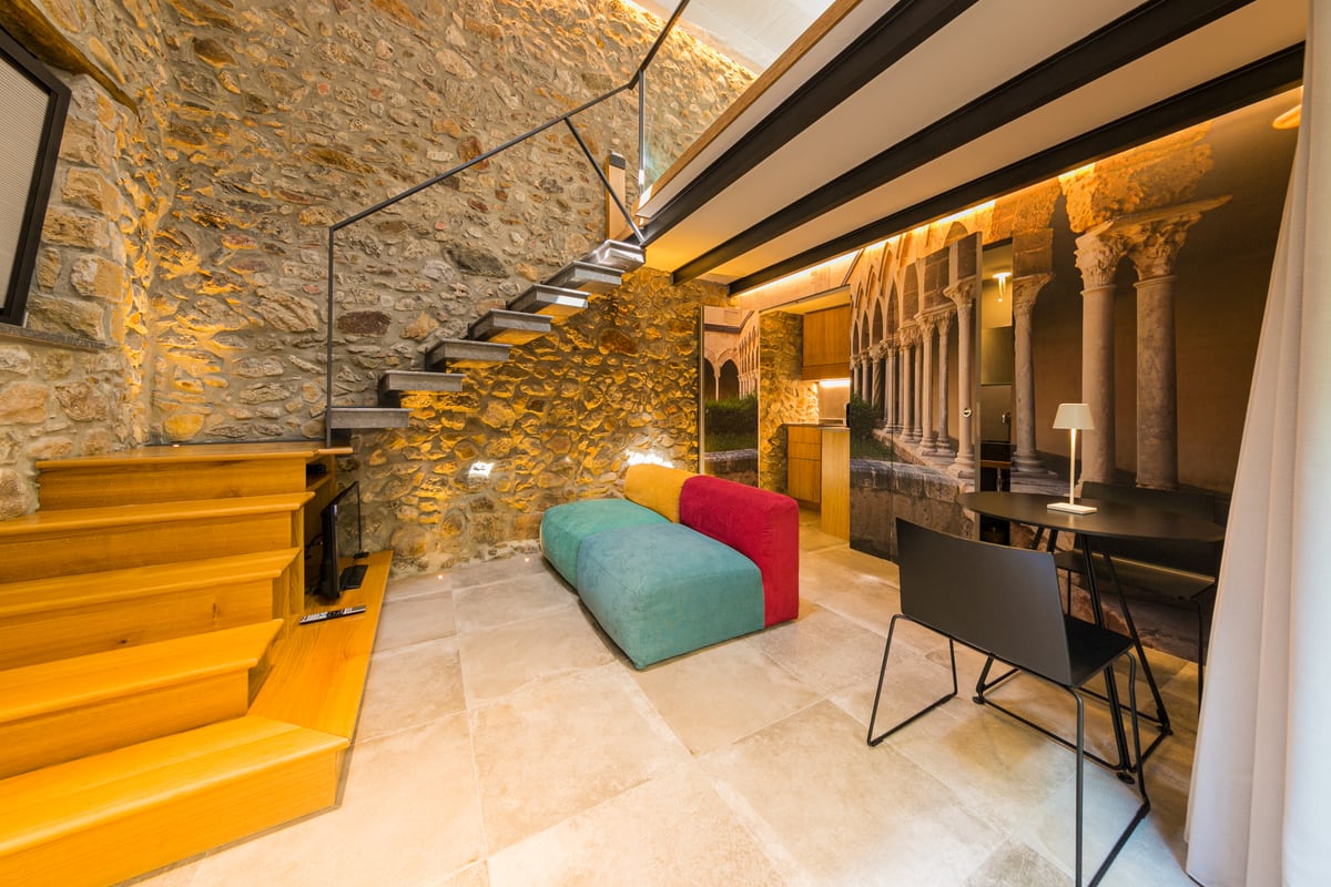 The living area with a colourful sofa, stone wall and stairs to the bedroom.
